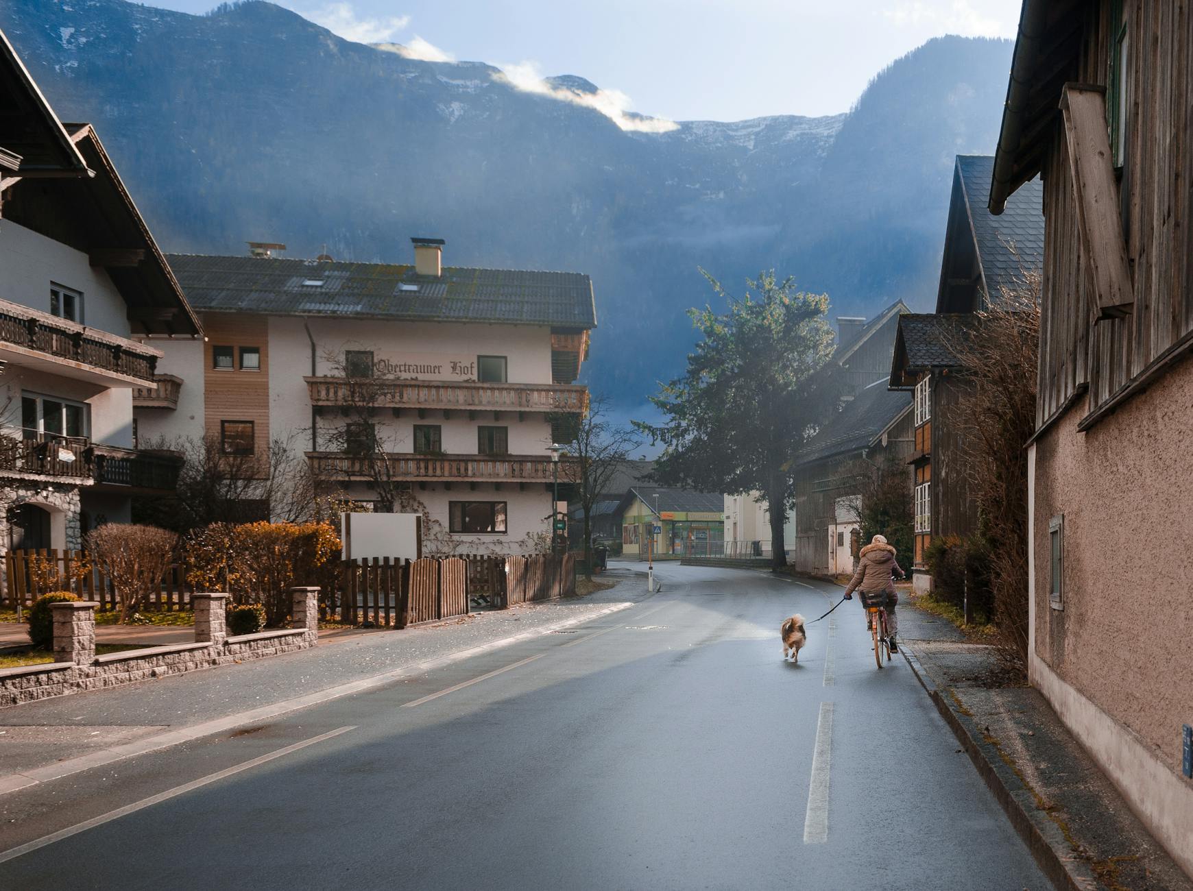 Kobieta na rowerze z psem na tle górskiej uliczki austriackiego miasteczka