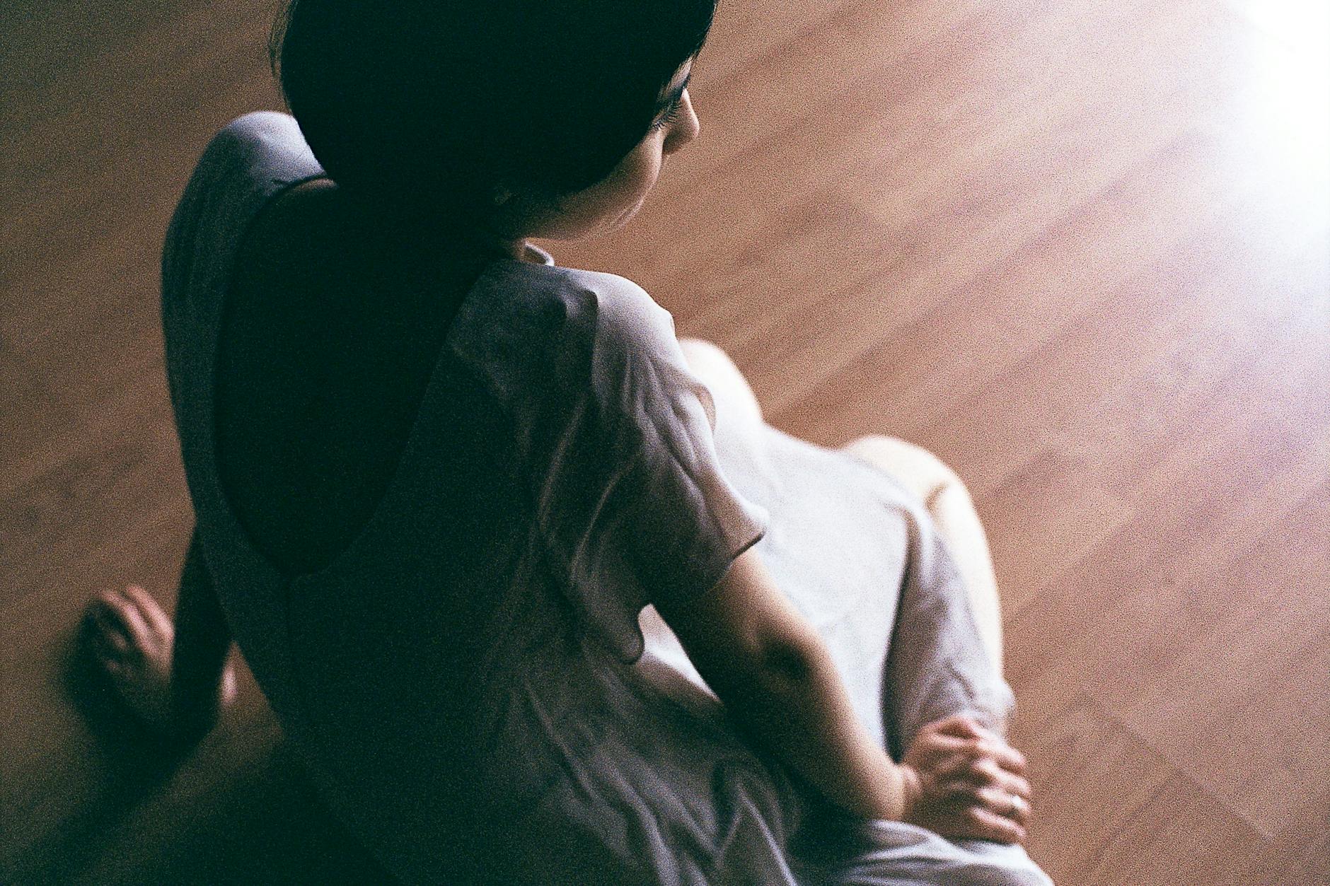 Kobieta w białej sukience siedzi na spokojnie oświetlonej podłodze drewnianej